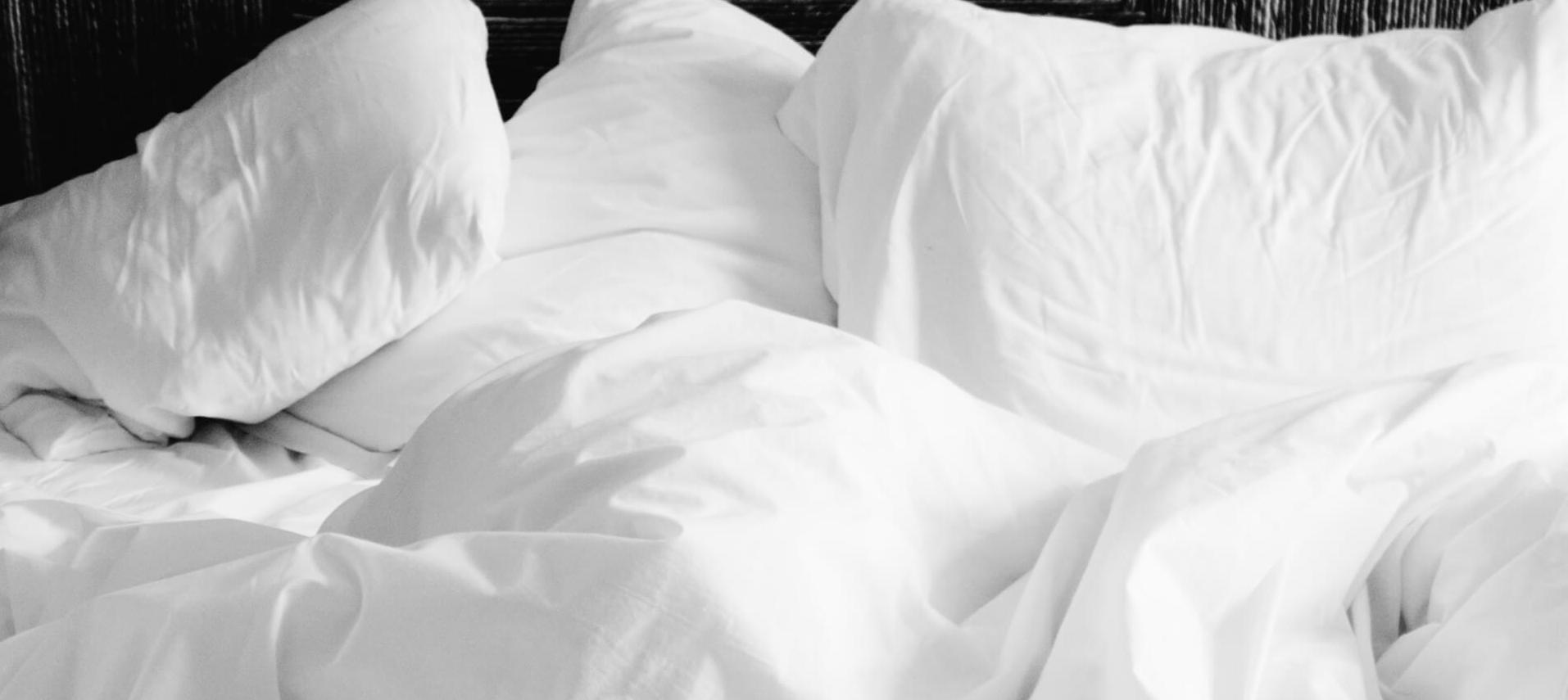 Weiße Bettwäsche auf einem Bett mit einer dunklen Wand im Hintergrund.