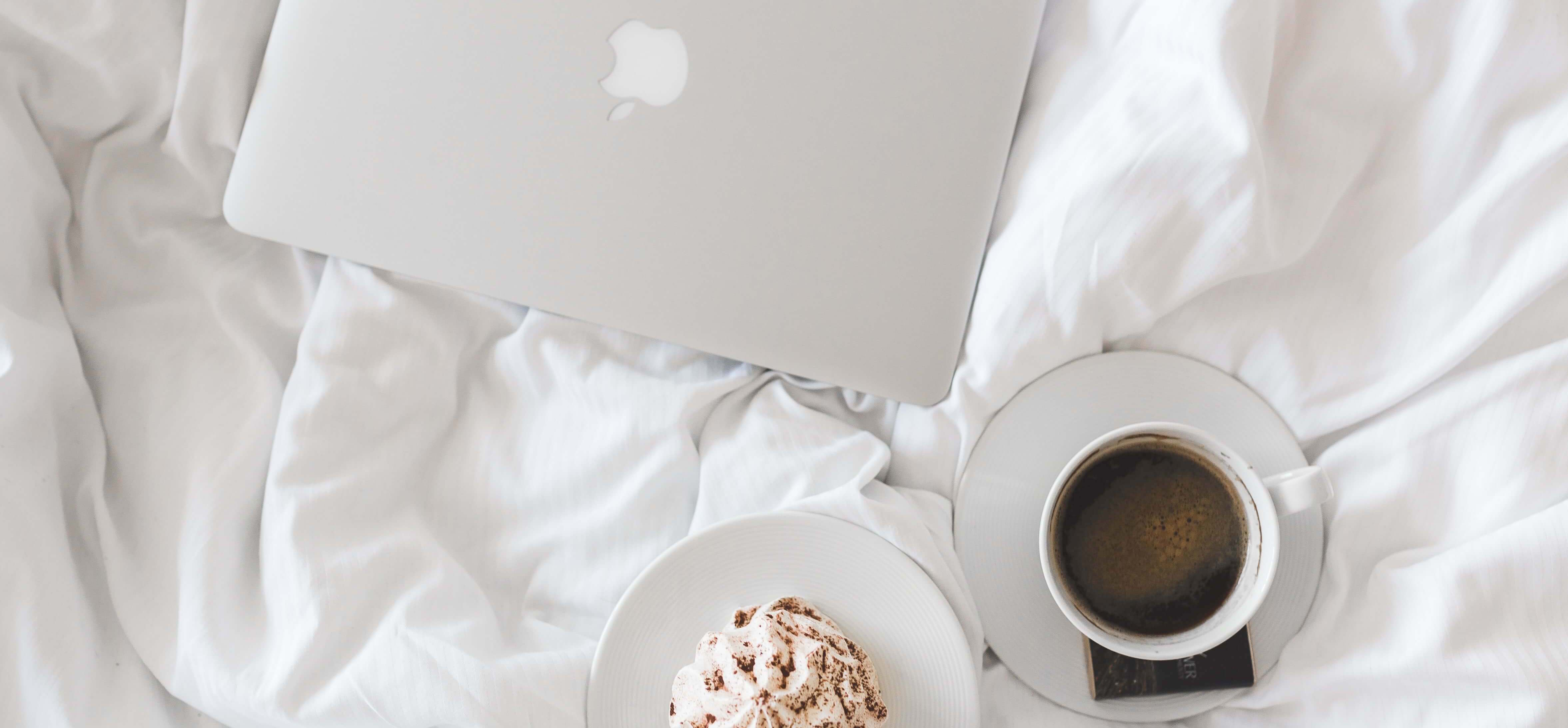 Weiße Bettwäsche mit Laptop, Kaffee und Kuchen